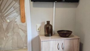 Una habitación con un armario de madera, un televisor montado en la pared y un jarrón sobre el mueble.