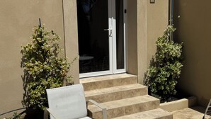 Eine Terrassenfläche mit einem weißen Stuhl, einem kleinen Tisch und einer Treppe, die zu einer Tür führt.
