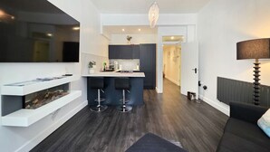 A modern kitchen with dark cabinetry, a central island with stools, a hanging light fixture, and a built-in shelf with a plant. - stylish ground floor apartment off Douglas promenade (Douglas)