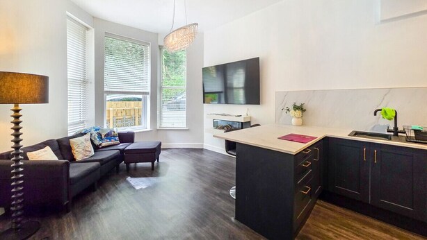 A modern kitchen with a large island, a dining area with a sofa and table, and a TV mounted on the wall. - stylish ground floor apartment off Douglas promenade (Douglas)
