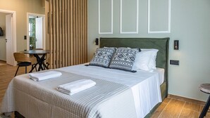 A neatly made bed with a green headboard, two patterned pillows, and a white blanket. - Ernest Suites Monastiraki (Athina)