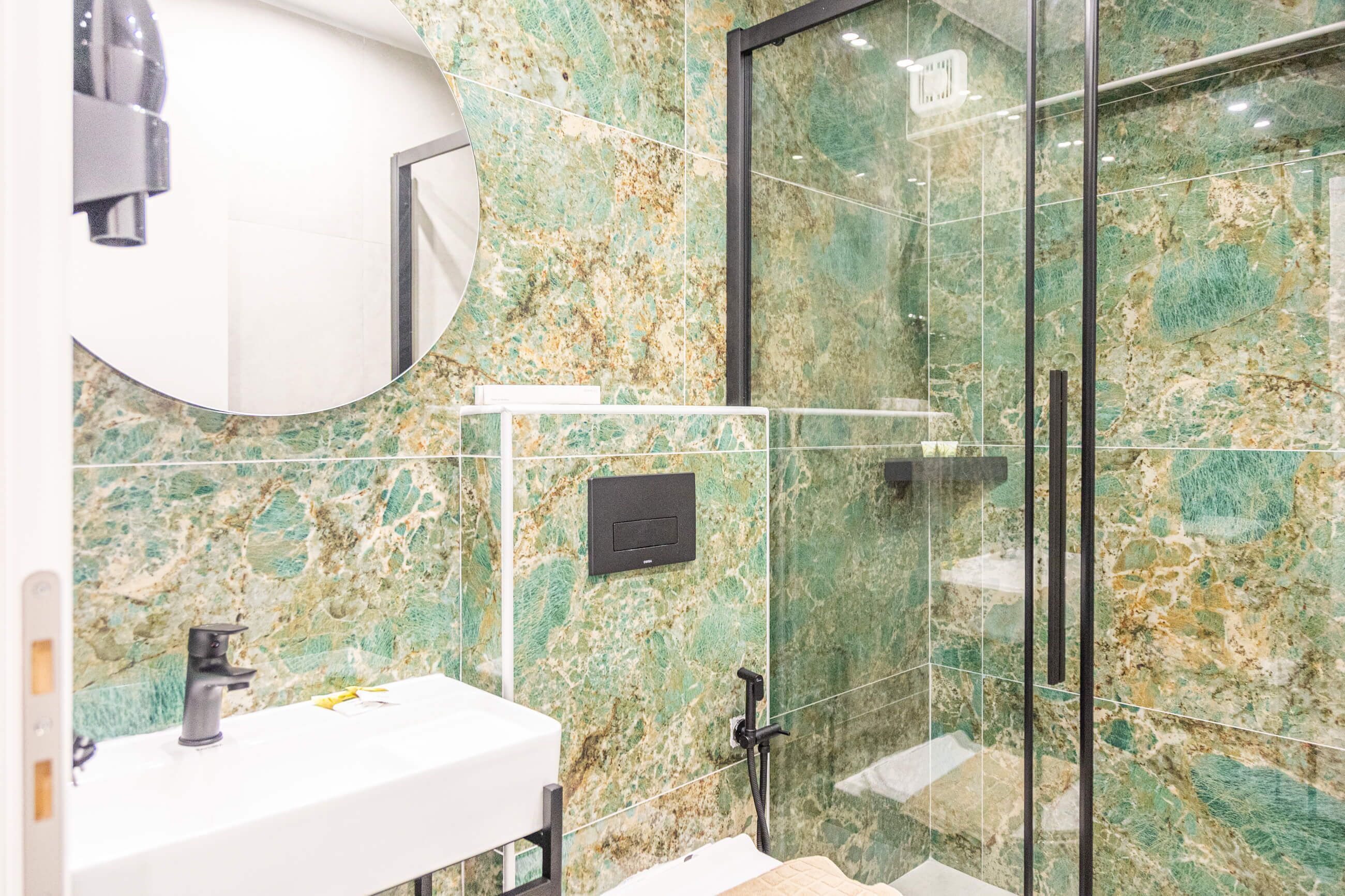 A bathroom with a white sink, a mirror, a glass shower enclosure, and a marble wall.