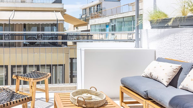 A balcony with wicker furniture, a woven basket, and a grey sofa with patterned cushions. - Ernest Suites Monastiraki (Athina)
