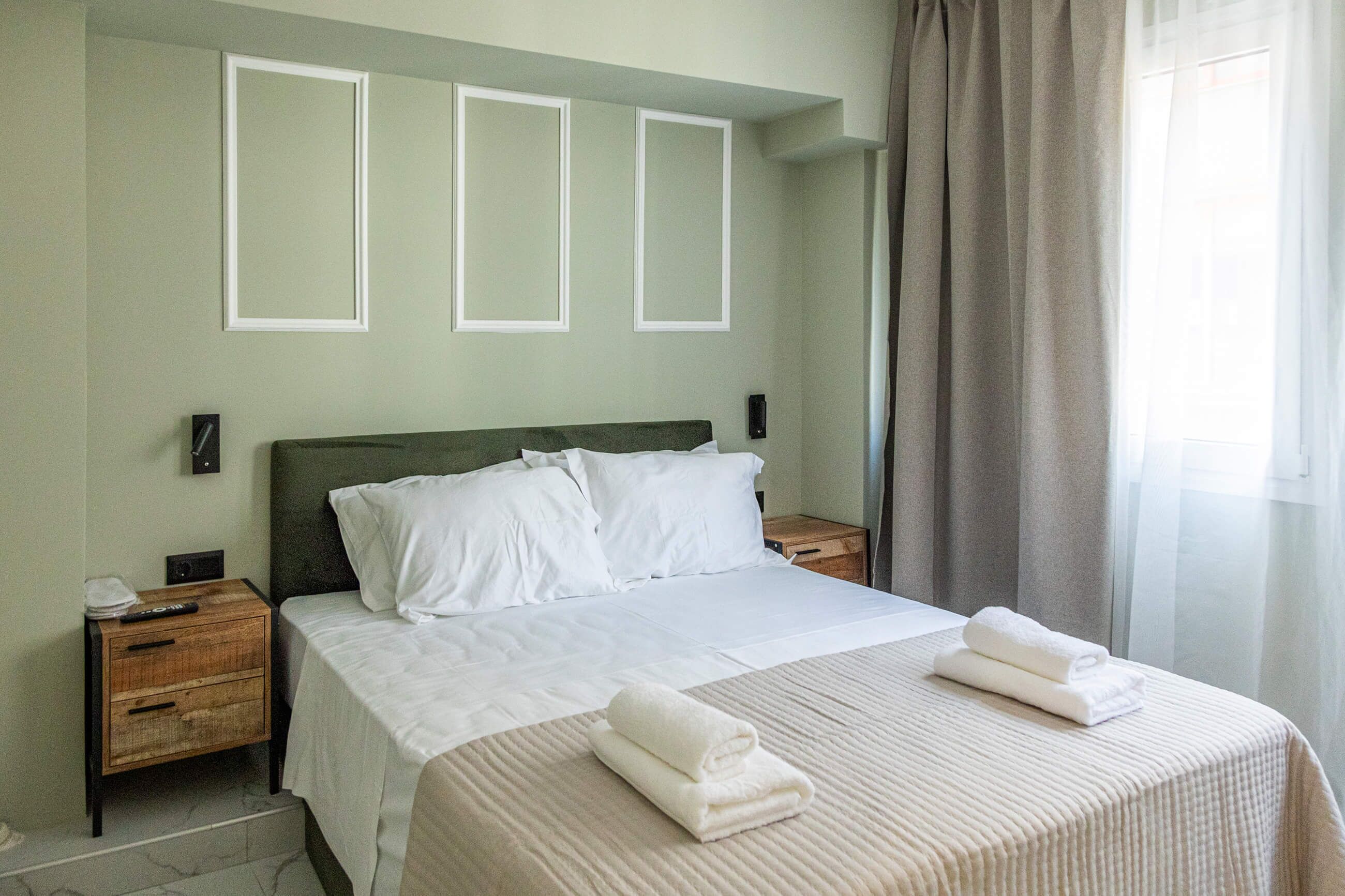 Une chambre d’hôtel avec un lit, des tables de chevet, un miroir et une fenêtre avec des rideaux.