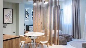 A modern living room with a round dining table, wooden chairs, a sofa, and a decorative screen. - Ernest Suites Monastiraki (Athina)