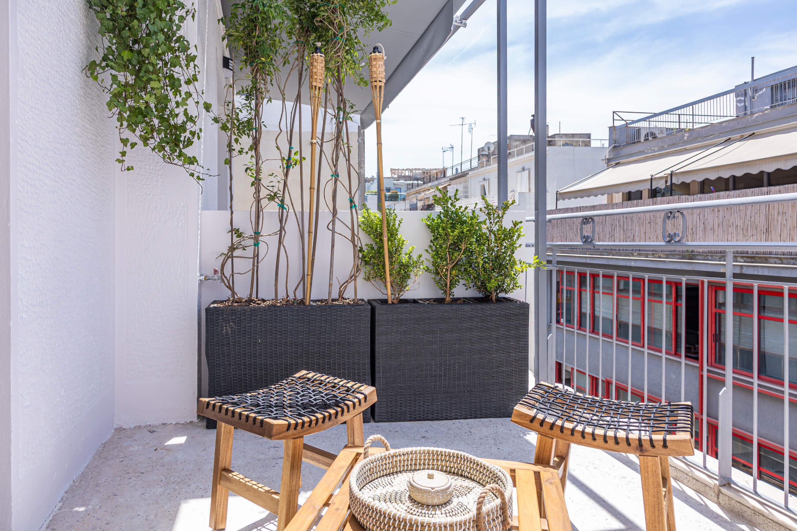 A balcony with wicker furniture, potted plants, and a view of a building with red windows.