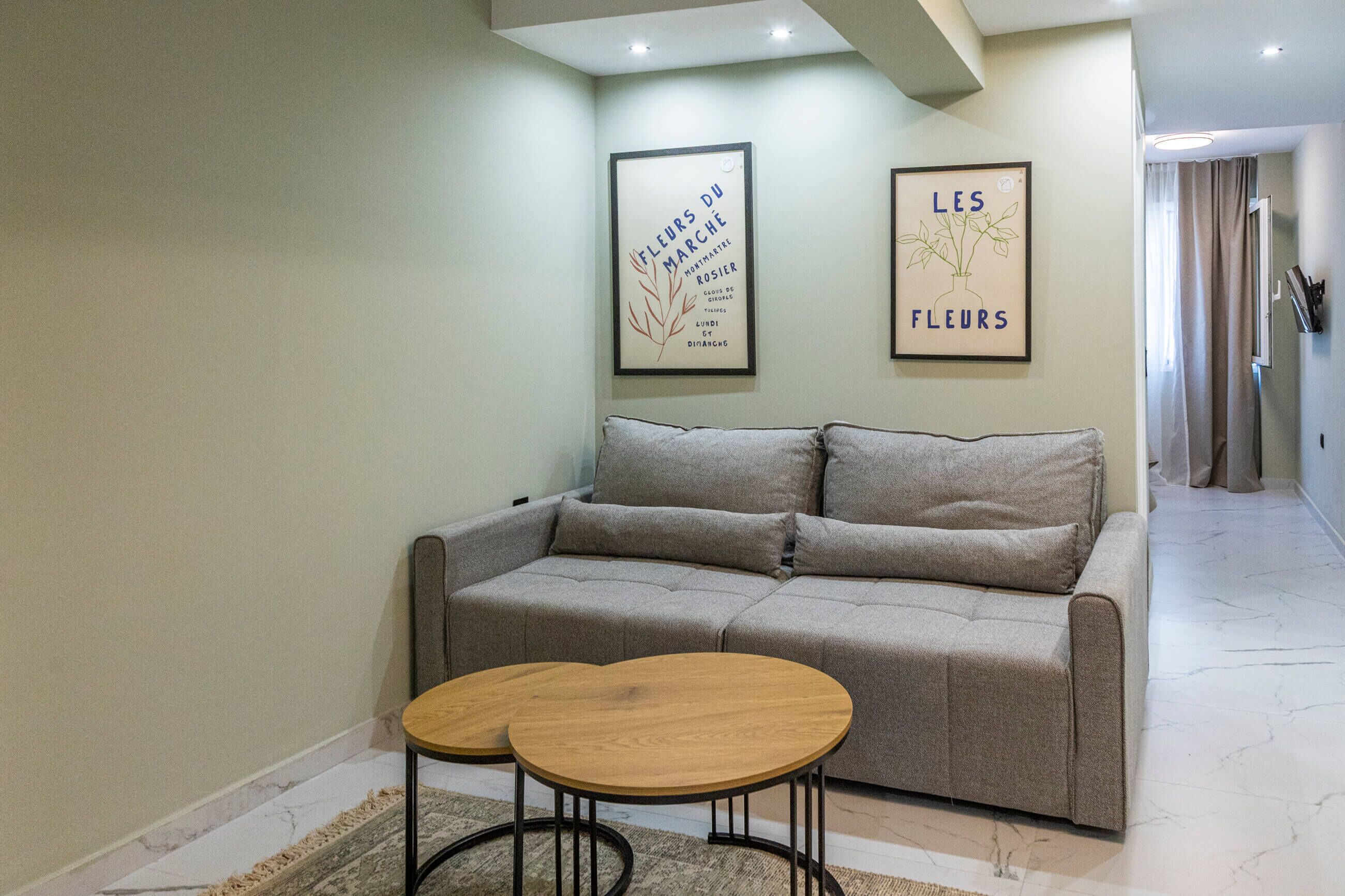 A modern living room with a grey sofa, two wooden side tables, and two framed artworks on the wall.