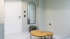 A room with a white door, a round wooden table with a black frame, a green ottoman, and a large mirror on the wall. - Ernest Suites Monastiraki (Athina)