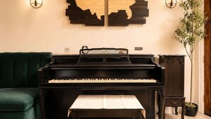 A black piano, a green sofa, a wooden cabinet, and a wall-mounted abstract art piece. - Regent Villa | Theatre | Hot Tub | Game Room | BBQ (Plano)