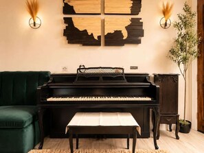 A black piano, a green sofa, a wooden cabinet, and a wall-mounted abstract art piece.