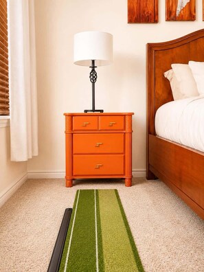 Un dormitorio con una cama de madera, una mesita de noche naranja con una lámpara y una alfombra verde a rayas.