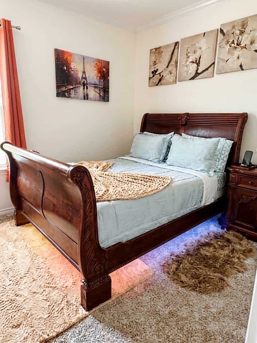 A bedroom with a wooden bed, a rug, and wall art.