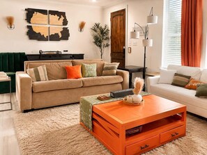Olohuoneessa on beige sohva, valkoinen sohva ja oranssi sohvapöytä.