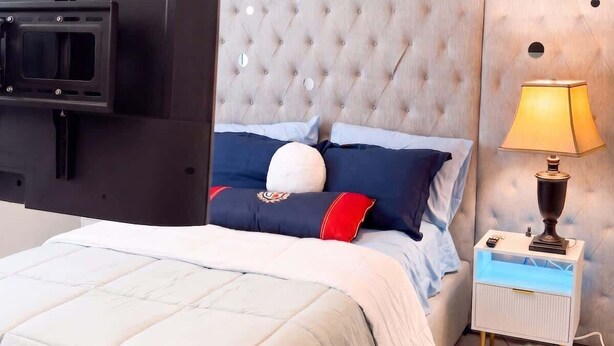 Ein Schlafzimmer mit Bett, Nachttisch, Lampe, Fernseher und einem gebürsteten Kopfschild.