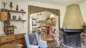 A rustic interior with a fireplace, wooden shelves, a dining area, and a wicker chair.