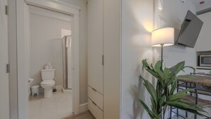 Un baño moderno con inodoro, bidé y ducha. Hay una zona de comedor con una mesa y sillas, y una planta.