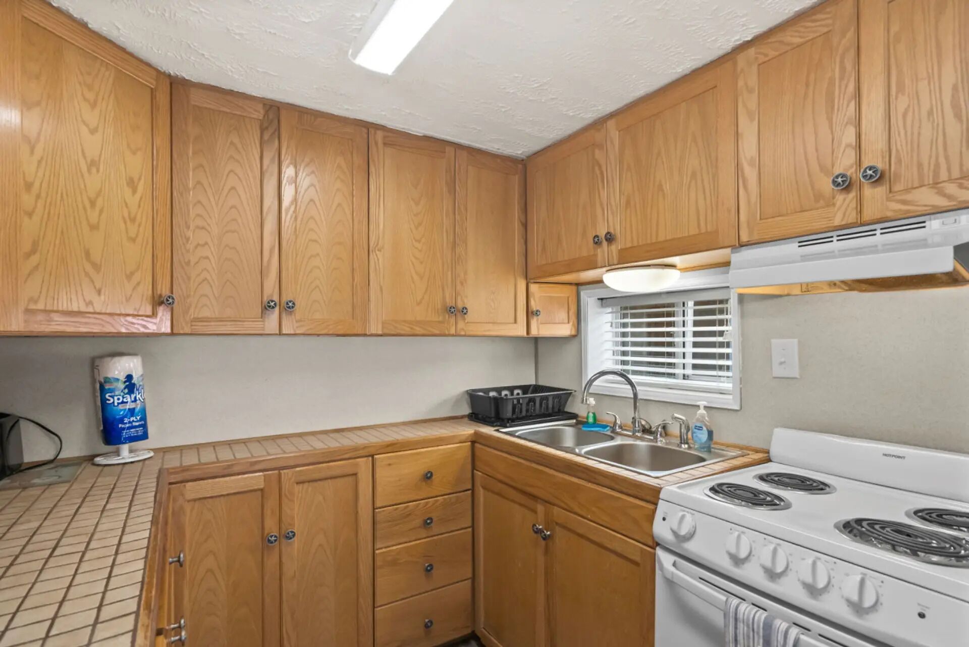 A kitchen with wooden cabinets, a stove, a sink, and a window with blinds.