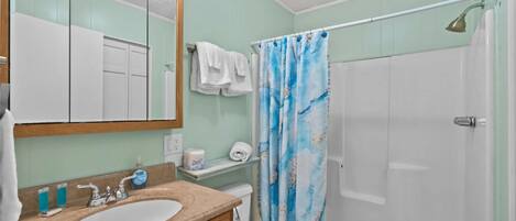 A bathroom with a sink, mirror, toilet, and shower.