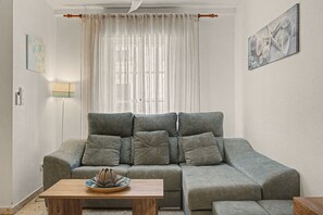 A living room with a grey sofa, a wooden coffee table, and a window with sheer curtains. - La Araucaria de Chipiona – Cozy Apartment with Private Parking and Terrace (Chipiona)