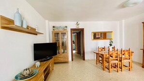 Ein Wohnzimmer mit Fernseher, Holzschrank, Esstisch, Stühlen und einem Schrank mit Glastüren.
