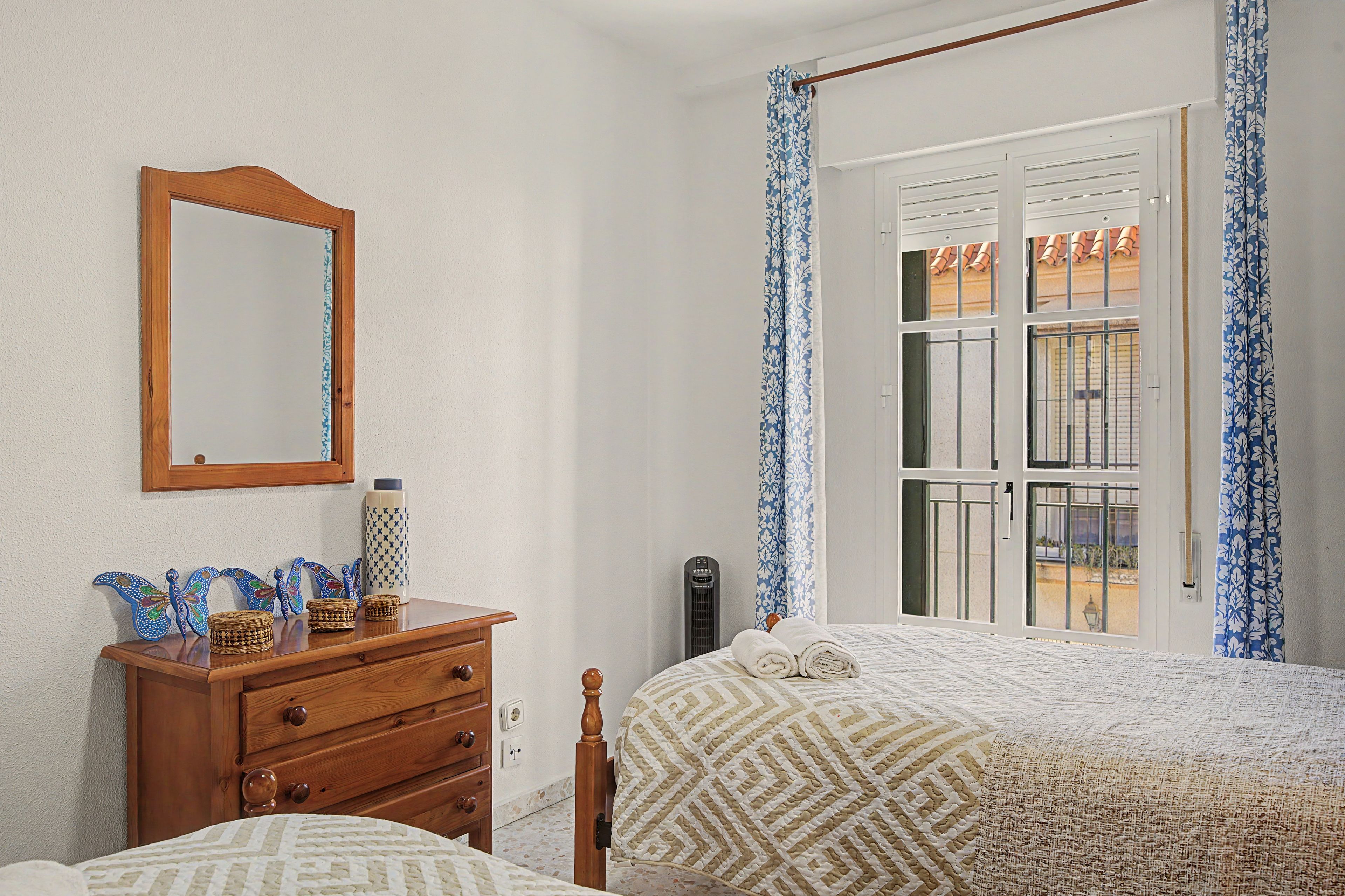 Een slaapkamer met een bed, een dressoir, een spiegel en een raam met gordijnen.
