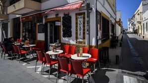 Ein Straßencafé mit roten Stühlen und Tischen, einem Schild für 'BAR VOKPIE' und einem Gebäude mit Balkonen unter blauem Himmel.