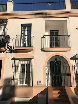 A building with multiple balconies, a large arched entrance, and a staircase leading to the entrance. - La Araucaria de Chipiona – Cozy Apartment with Private Parking and Terrace (Chipiona)
