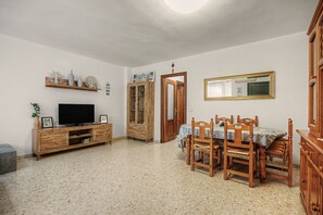Una sala de estar con televisor, muebles de madera, una mesa de comedor con sillas y un espejo en la pared.