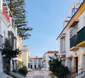 A narrow street lined with white buildings, balconies, and a clear blue sky. - La Araucaria de Chipiona – Cozy Apartment with Private Parking and Terrace (Chipiona)