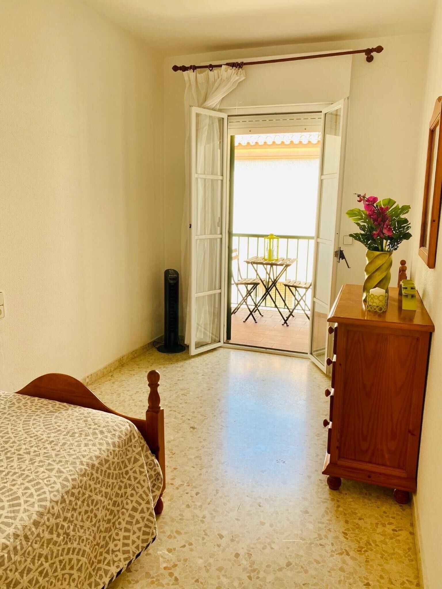 Een slaapkamer met een bed, een houten dressoir en een balkon met een tafel en stoelen.