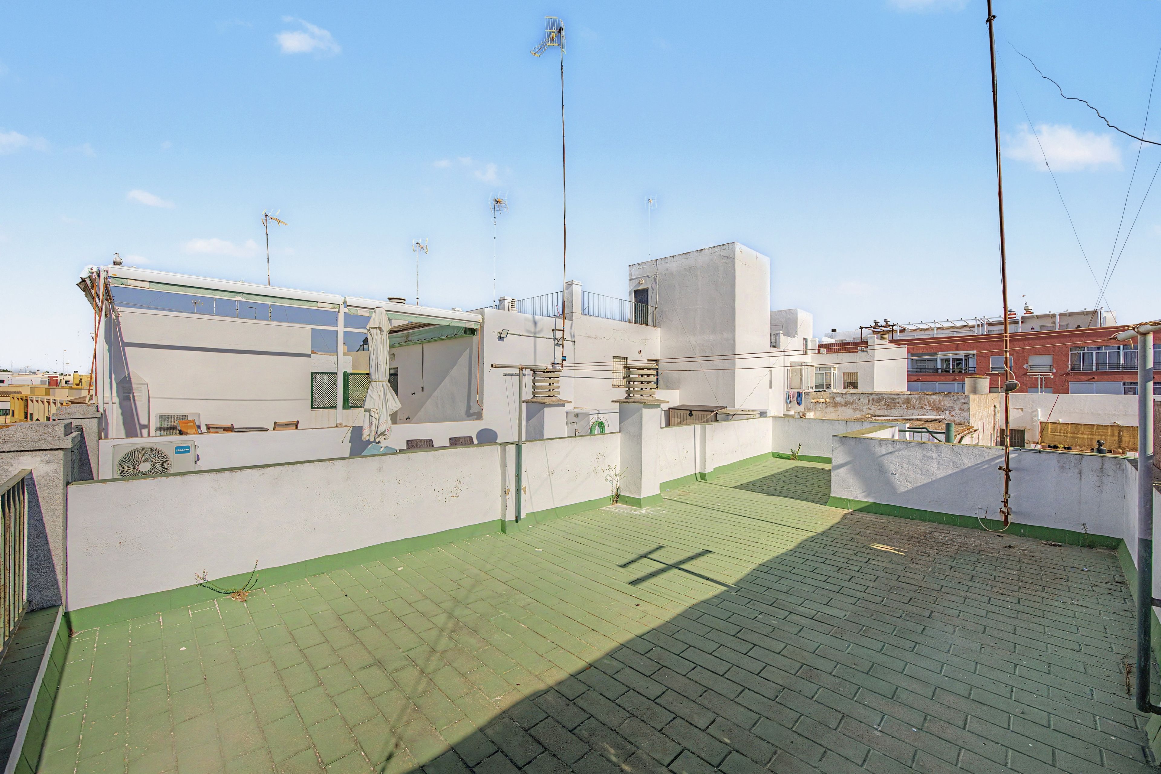 A rooftop terrace with a green floor, white walls, and a metal structure.