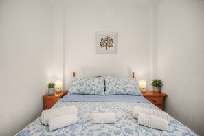 A neatly made bed with a patterned bedspread, two pillows, and two bedside tables with lamps and potted plants. - La Araucaria de Chipiona – Cozy Apartment with Private Parking and Terrace (Chipiona)