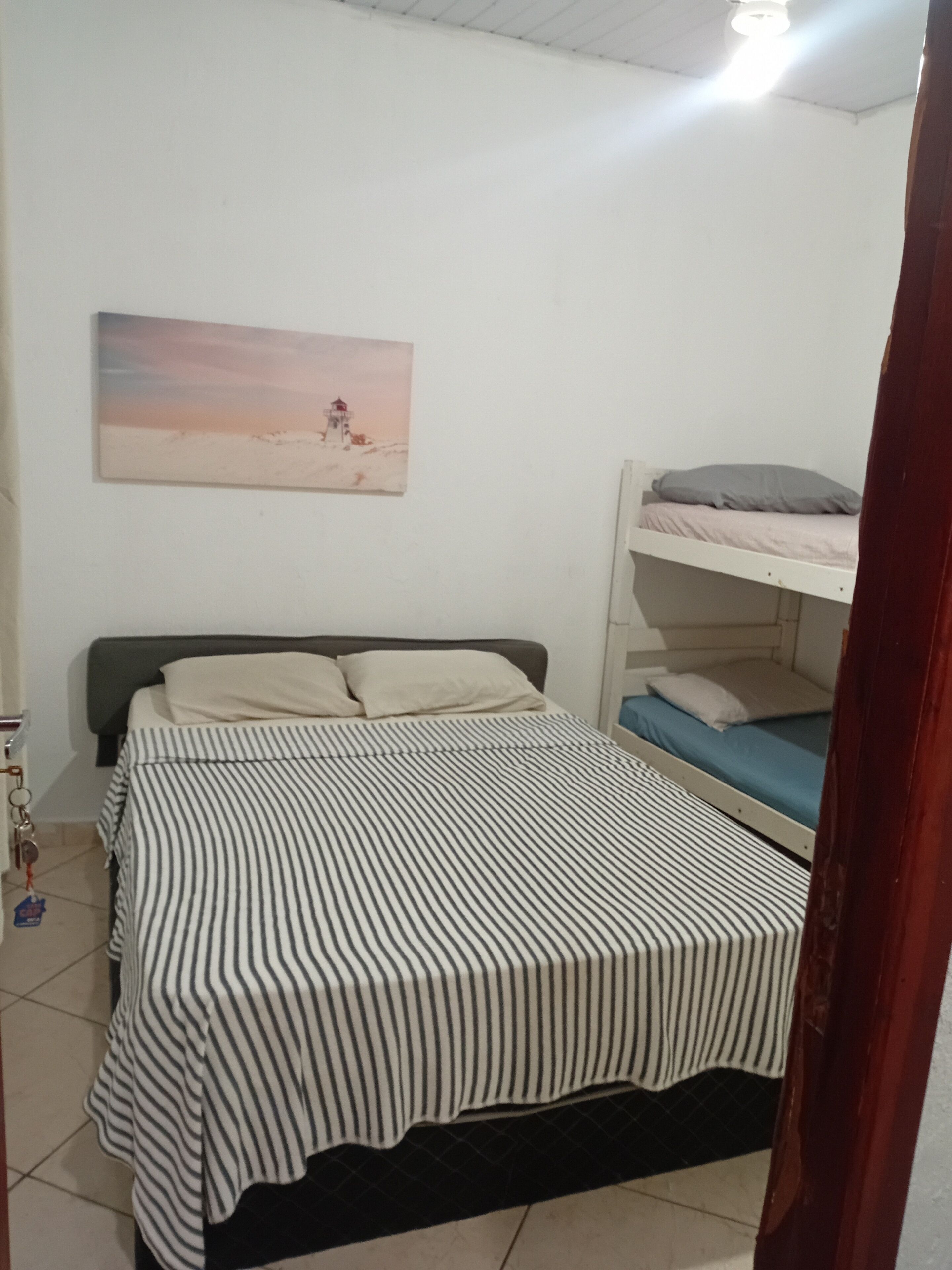 A bedroom with a bunk bed, a striped bedspread, a painting on the wall, and a tiled floor.