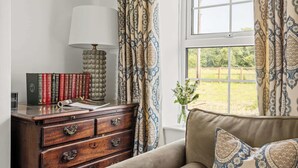 A room with a wooden dresser, books, a lamp, and a window with curtains. - Pet-Friendly Cottage w/ Garden Near Malton (Malton)
