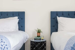 Een slaapkamer met twee bedden, een klein rond tafeltje met een plant en een glas water.
