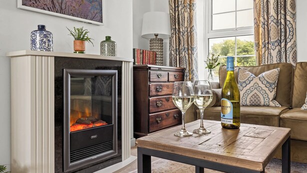 A cozy living room with a fireplace, a sofa, a coffee table with wine glasses and a bottle, and a bookshelf. - Pet-Friendly Cottage w/ Garden Near Malton (Malton)
