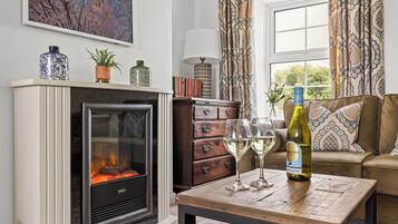 Un salon chaleureux avec une cheminée, un canapé, une table basse avec des verres à vin et une bouteille, et une bibliothèque.