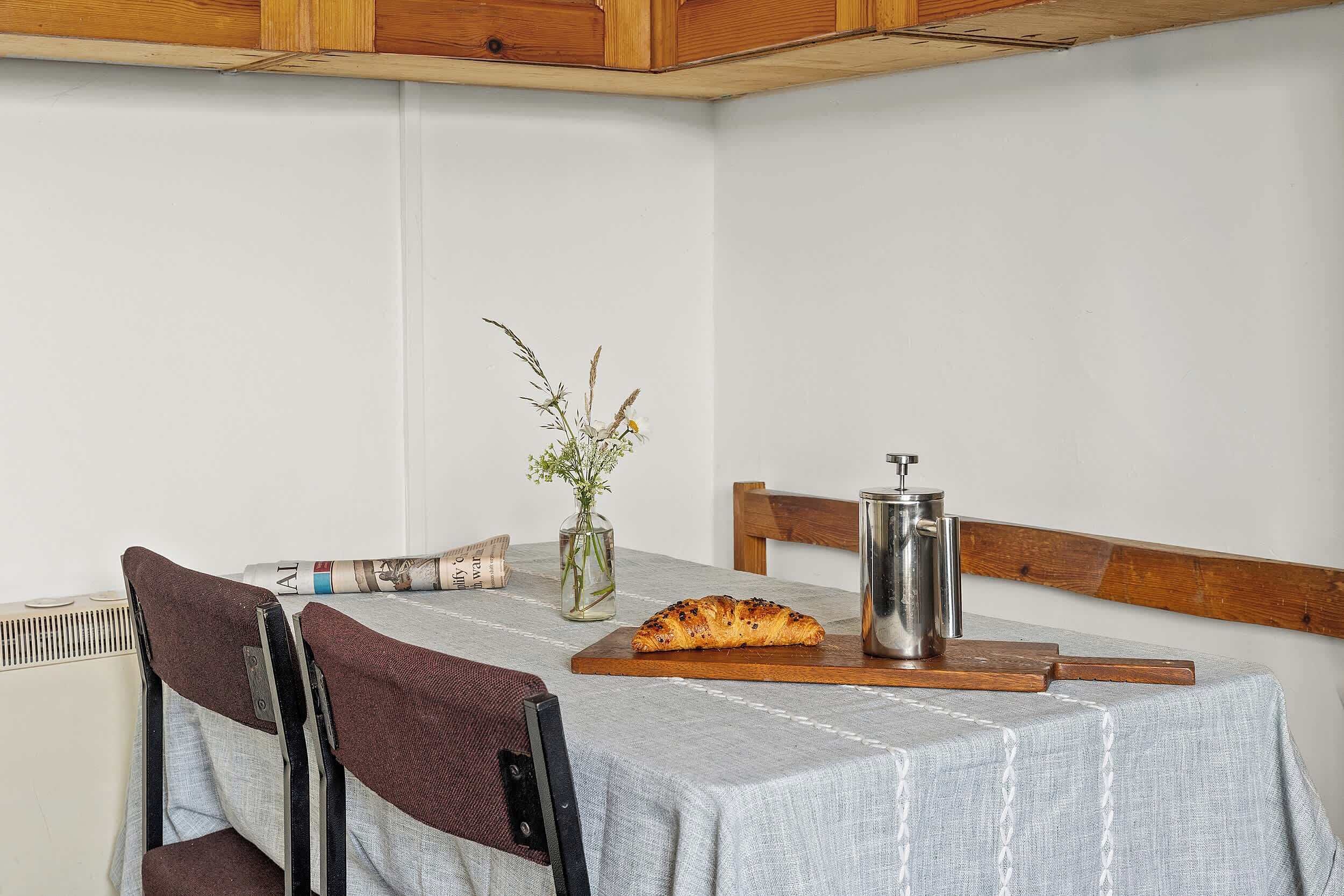 A dining table with a metal pitcher, a loaf of bread, and a vase with dried plants.