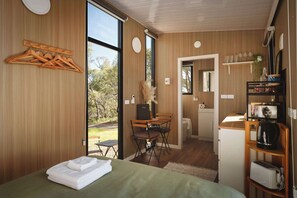 A room with a bed, a desk, a chair, a small kitchenette, and a view of the outdoors.