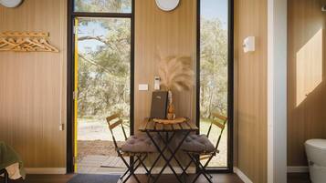 A modern interior with a wooden dining table, two cushioned chairs, a small wooden bench, and a view of the outdoors through large glass doors.