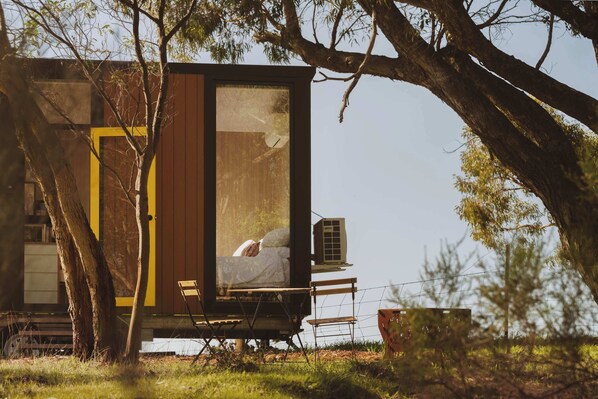 Una casa en el árbol con cama, una pequeña mesa y un equipo de aire acondicionado.