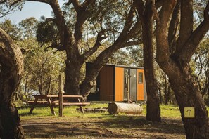 Eine kleine Holzhütte mit einer Holzterrasse und einem Picknicktisch, umgeben von großen Bäumen.