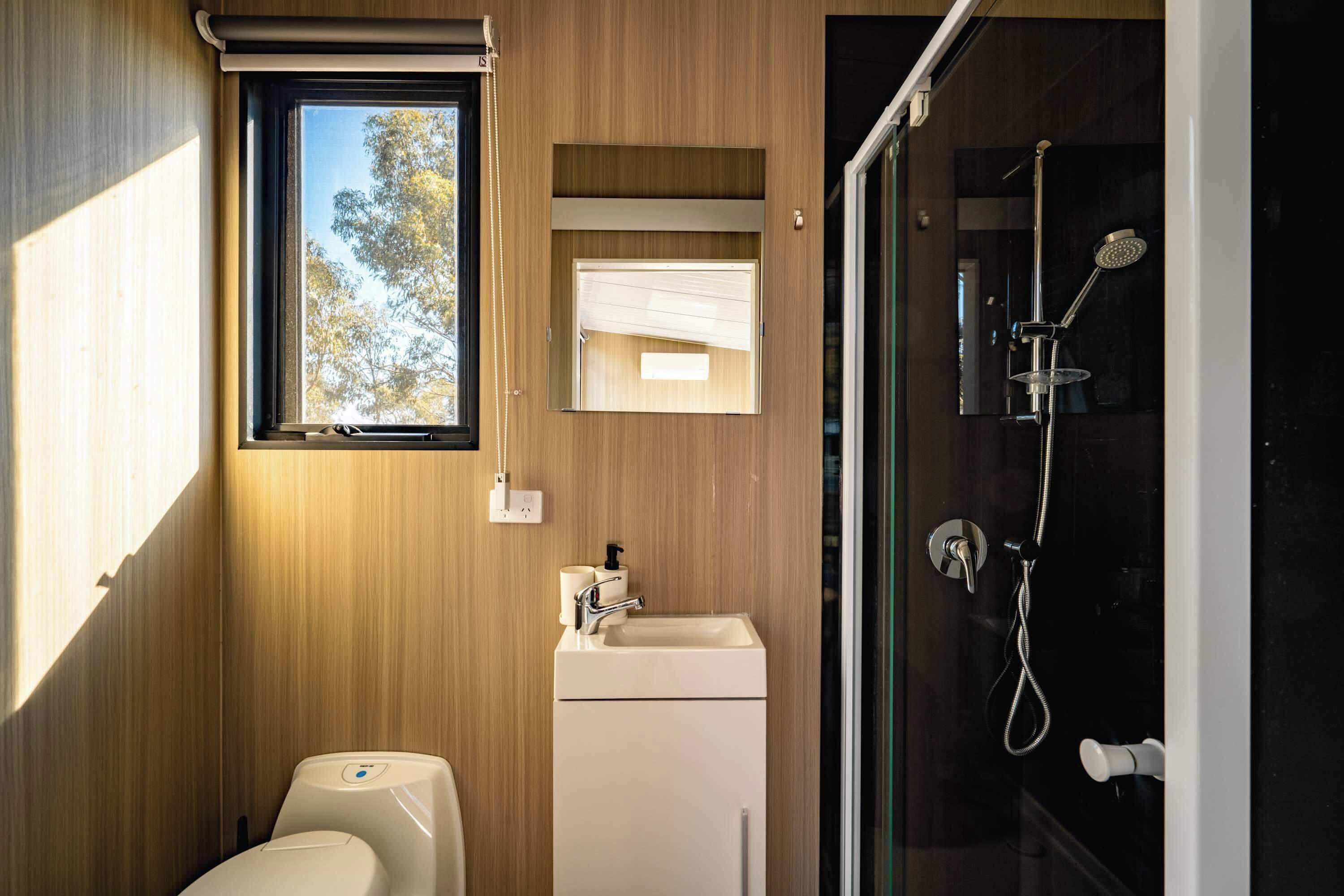 A modern bathroom with a wooden wall, a window, a sink, a toilet, and a shower.