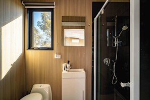 Un baño moderno con pared de madera, ventana, lavamanos, inodoro y ducha.