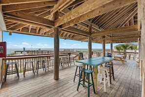 Eine Holzterrasse mit Tischen und Hockern mit Blick auf einen Strand.