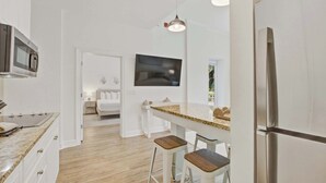 Une cuisine moderne équipée d’un réfrigérateur en acier inoxydable, d’un four à micro-ondes et d’un comptoir en granit. On y trouve deux tabourets de bar et une petite table avec une lampe.