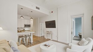 Un salon moderne comprenant un canapé, une table basse et un coin cuisine avec des tabourets de bar.
