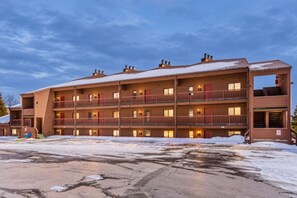 Un hôtel à plusieurs étages doté de balcons, d’un parking et dont le toit est recouvert de neige.