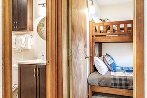 Ein Stockbett mit karierter Decke, eine Holztür, ein Waschbecken und ein Handtuchhalter in einem Zimmer.