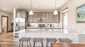 Una cocina moderna con una isla central, taburetes de bar, electrodomésticos de acero inoxidable e iluminación colgante.